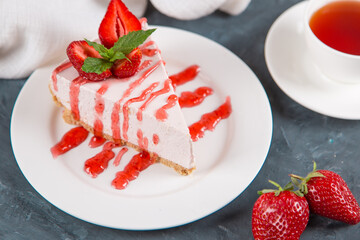 Sweet breakfast, tea and delicious cheesecake with fresh strawberries and mint, homemade recipe without baking, on dark blue stone table. Copy space.