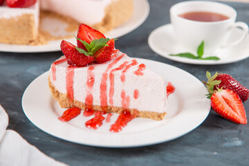 Sweet breakfast, tea and delicious cheesecake with fresh strawberries and mint, homemade recipe without baking, on dark blue stone table. Copy space.