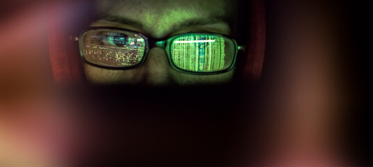 hacker at computer data reflecting in eyeglasses