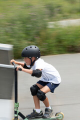 A cute little boy rides a scooter in a skatepark.