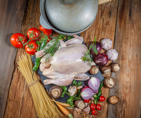 A set of fresh products for cooking chicken dishes.Chicken, carrots, mushrooms, onions, Bay leaf, tomatoes, pepper, dill, parsley, pasta, cast-iron pot, on a wooden table, close-up, top view