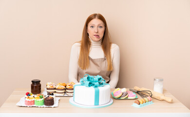 Obraz na płótnie Canvas Young redhead woman with a big cake having doubts and with confuse face expression