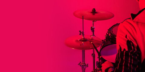 Fototapeta na wymiar Cropped. Young inspired and expressive musician, drummer performing on gradient colored background in neon light. Concept of music, hobby, festival, art. Joyful artist, colorful, bright portrait.