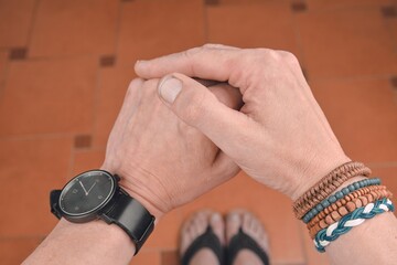 Fototapeta premium Man wearing a bracelet made of rope, wood, leather, beads and colored rope sack. Black watch on man hand. Hipster fashion on tiled flooring background