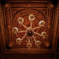 Beautiful crystal Chandelier lamp hanging from a wooden luxurious decorated ceiling of a room. Close up view with a glamorous background.