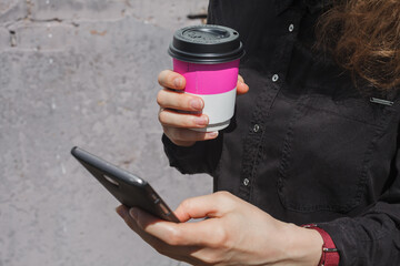 Girl with coffee cup holds smartphone in hand close-up