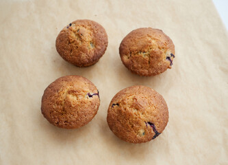 Freshly baked muffins with berries on a light brown crafted parchment, top view. Perfect tasty pastry for breakfasts, snacks, lunch or teatime. Homemade sweets cooking and baking concept.