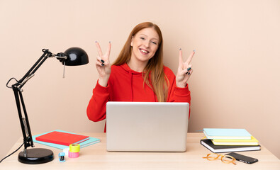 Young student woman in a workplace with a laptop showing victory sign with both hands