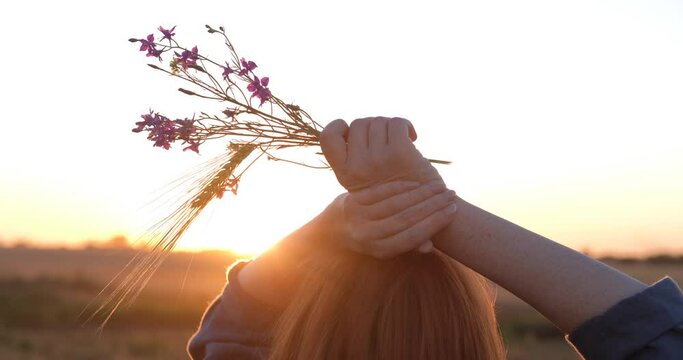 Young redhead woman in beautiful boho dress relaxing in the field during foggy sunset, female outdoors with bouquet in hands