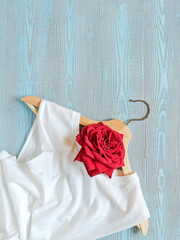 Flower composition. Layout of a wooden hanger, white cotton T-shirt and red roses. Blue wooden background. Template for sales, discounts, a new collection of clothes. Flat lay. Top view. Copy space.