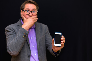 Middle age 40s business man showing smartphone screen over black background