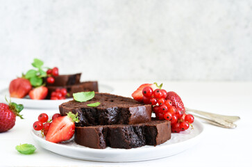Chocolate muffin with strawberries and currants on a light concrete background. Pieces of cake. Brownie pie.