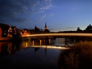 Fototapeta premium Nachtszene mit dunkelblauen Himme, eine beläuchtete Brücke verläuft über dem Fluß und spiegelt sich im Wasser