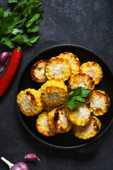 Baked hot corn with butter in a cast-iron pan on a black background. View from above.