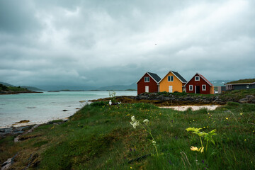 Fototapeta na wymiar Characteristic colorful yellow and red wooden huts. Summer houses (cabin) on the azure sea, beautiful beach in the Sommaroy island, northern Norway. Horizontal orientation.