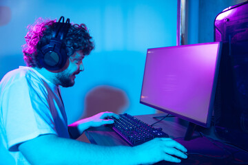 Cyber sport. Copyspace on monitor, screen. Fully concentrated professional gamer playing important match. Caucasian man practicing before tournament alone in neon light. E-sport, gamer, streamer.