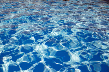 Clear shiny and warm blue water in the pool reflected in it by the rays of the sun in anticipation of tourists. Vacation and travel concept. Advertising space