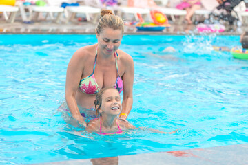 Obraz na płótnie Canvas Mom teaches daughter to swim in the pool