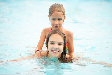 Fototapeta na wymiar Two cute little sisters girls swim in the pool during vacation on a sunny warm summer day. The concept of the long-awaited vacation. Advertising space
