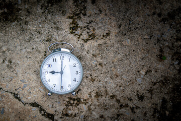 Gray alarm clock on cement floor.