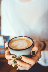 Woman holding a almond milk cappuccino, with latte art of a heart in the foam. Vintage coffee barista concept. 