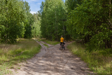 Obraz premium Healthy lifestyle - a cyclist rides a bicycle on a trail in a beautiful summer forest. Reunion with nature. Digital detox.