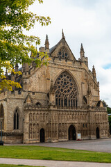 Fototapeta na wymiar Exeter Cathedral side on image with cloudy sky in the background and framed by green trees and grass in the foreground