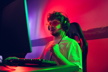 Fototapeta premium Cyber sport. Fully concentrated professional cybersport gamer playing important match. Caucasian male model practicing, training before tournament alone in neon light. E-sport, gamer, streamer.