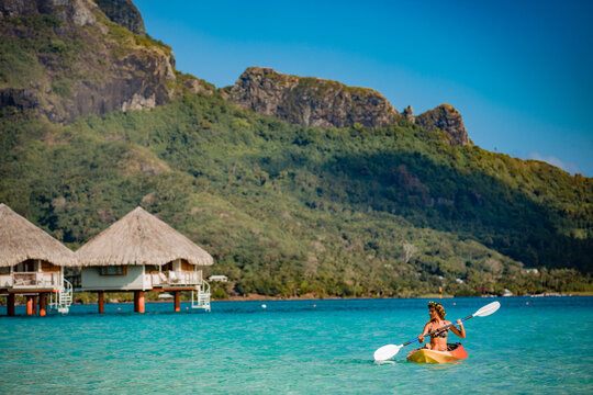 Woman paddling a kayak by the tropical beach.