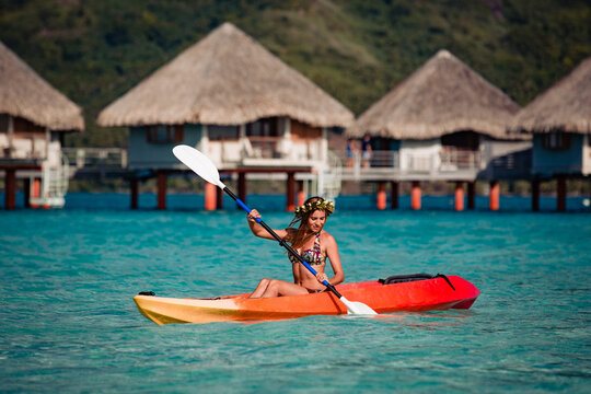 Woman paddling a kayak by the tropical beach.