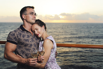 handsome man and beautiful woman standing with glasses white wine on cruise ship at nice sunset  background