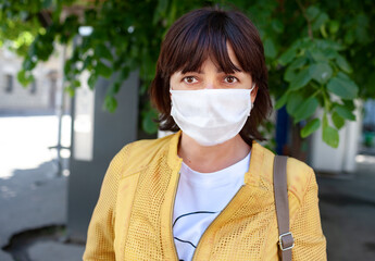 Portrait of an unidentified young woman in a mask posing outdoors during a coronovirus pandemic on a sunny warm summer day. Microbe protection and health concept