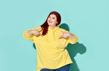Foxy-haired curvy young female winking joyfully and pointing on herself with both hands. Cropped...