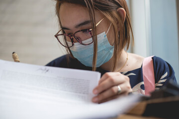 An asian lady wearing a surgical mask signs some printed documents. New normal concept.
