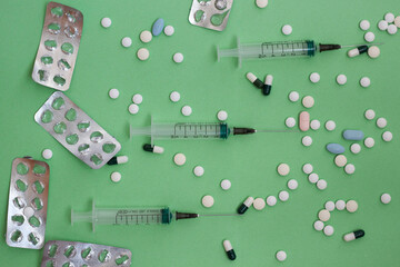 Three syringes with a needle empty lying on a green background and a lot of tablets and packages around