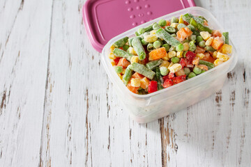 Healthy food is frozen. Containers frozen vegetable mixture of pepper, carrots, corn and peas. Copy space.