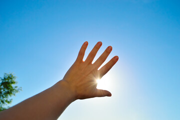 silhouette of a female hand on a background of blue sky and bright sun at sunset