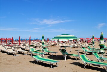 Fototapeta na wymiar Colorful chairs in a sandy beach in Rimini, Italy. Relax vacations in an italian beach
