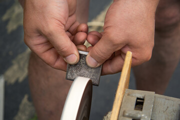 Men's hands hold a piece of metal, which is sharpened with the help of a grinding electric circle