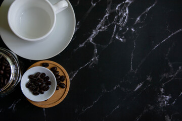 White coffee cups and roasted coffee beans With a glass jar filled with coffee beans On a black marble background