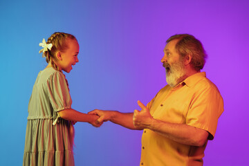 Playing, laughting. Senior man spending happy time with granddaughter in neon. Joyful elderly lifestyle, family, childhood, tech concept. Enjoying time with fun and happiness. Copyspace. Sincere happy