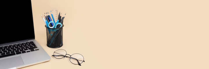 Laptop, glasses, metal bucket with stationery on a beige background. Banner with place your design.