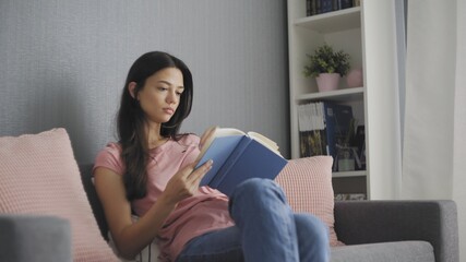 Beautiful young woman reading a sad book while sitting on sofa