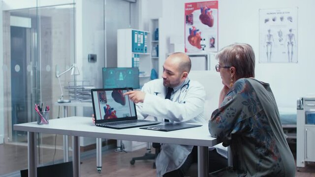 Young male doctor explaining possible heart disease to elderly retired old woman patient. Heart disease problems presented by cardiologist cardiology, heart attach. Health care in modern private