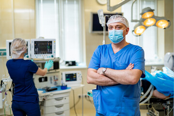 Doctor stands crosshands in medical mask. Medical team on background. Doctor in glasses with medical mask on face. Close up shot.