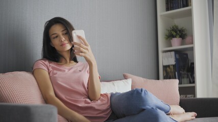 Beautiful woman taking selfie using phone while sitting on sofa at home
