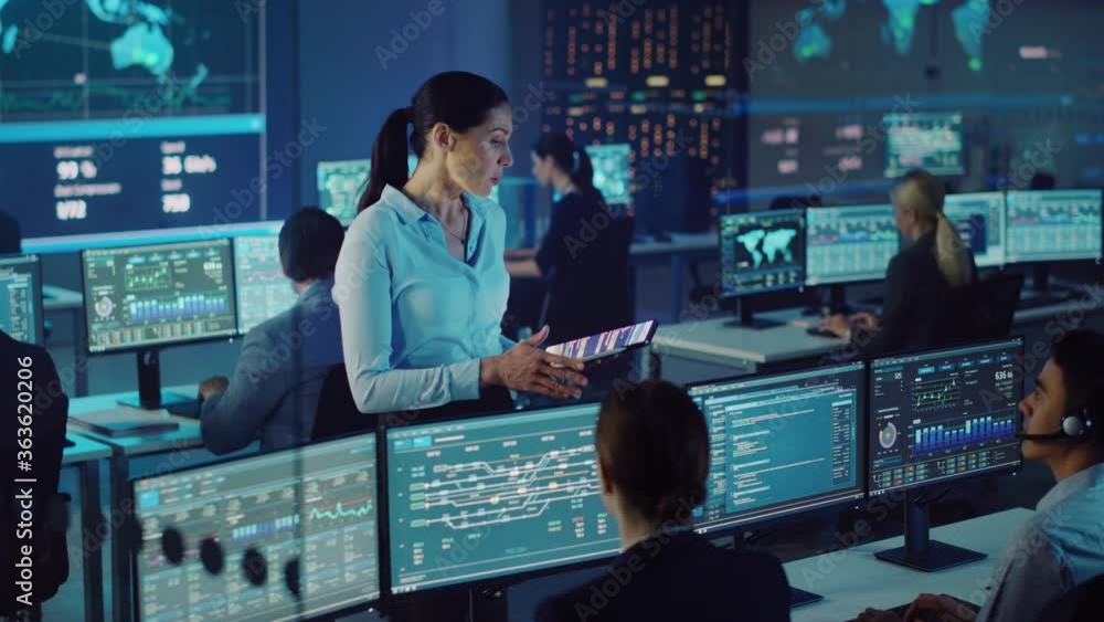 Poster Female Project Leader with Tablet Computer Talks to Young Data Science Engineers and Checks Up on Their Work Progress. Telecommunications Control Monitoring Room with a Global Map on Big Screen.