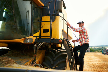 Harvester machine driver climbing into a cab to harvest his wheat field. Farmer getting in combine...
