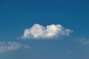Lonely white cumulus cloud in a blue summer sky. Nature background.