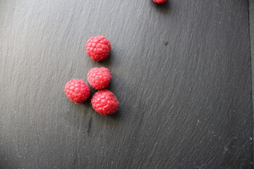 food background red raspberries are scattered lying on a gray stone black background there is a...
